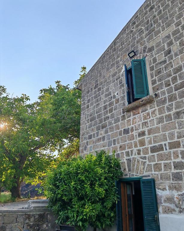 a brick building with green shutters and a bush at Gli Ulivi del Nonno - Casale immerso nel verde a pochi chilometri dalla Reggia - in Caserta