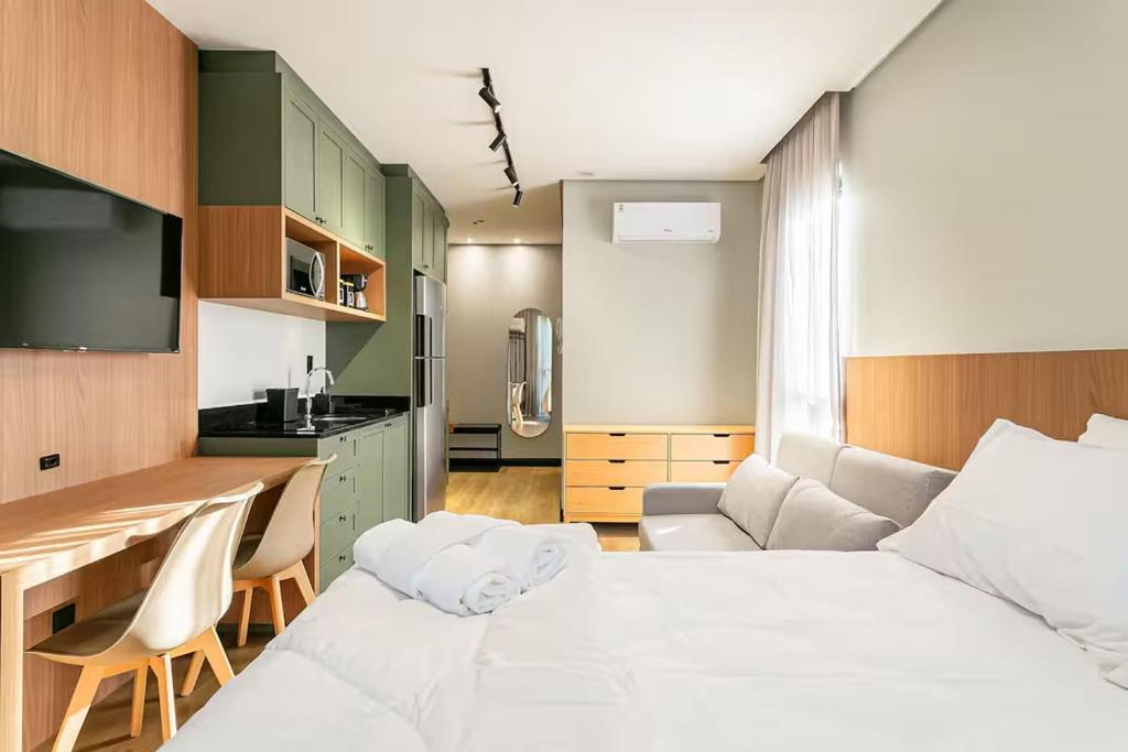 a bedroom with a white bed and a kitchen at Loft Completo com Piscina Aquecida 250m da Vila Germânica in Blumenau