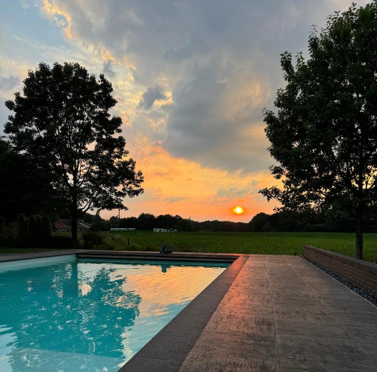 a swimming pool with a sunset in the background at B & B De Allee in Almelo