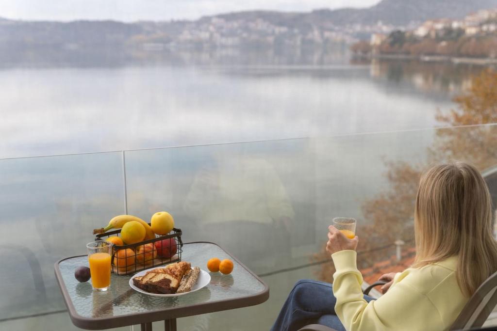 a woman sitting at a table with a plate of food and orange juice at Lakeview Sunset Kastoria in Kastoria