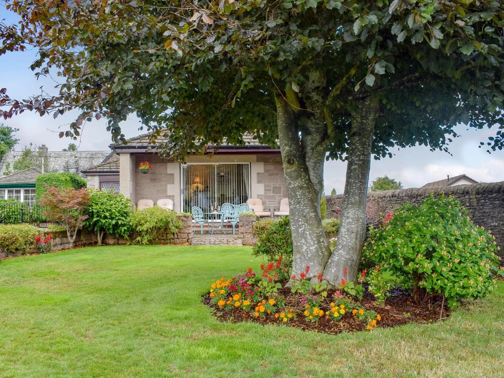 a house with a tree and flowers in the yard at Craigrossie Cottage in Auchterarder