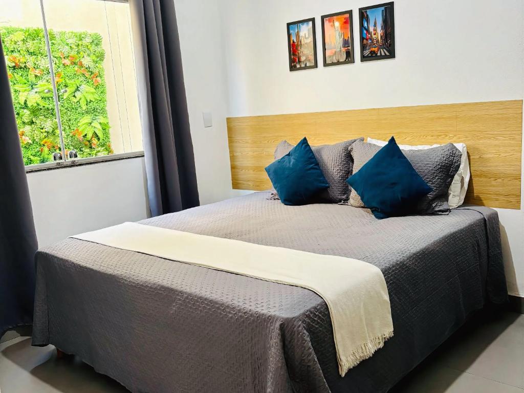 a bedroom with a bed with blue pillows and a window at VOER - BR Flat Hospedaria in Sete Lagoas
