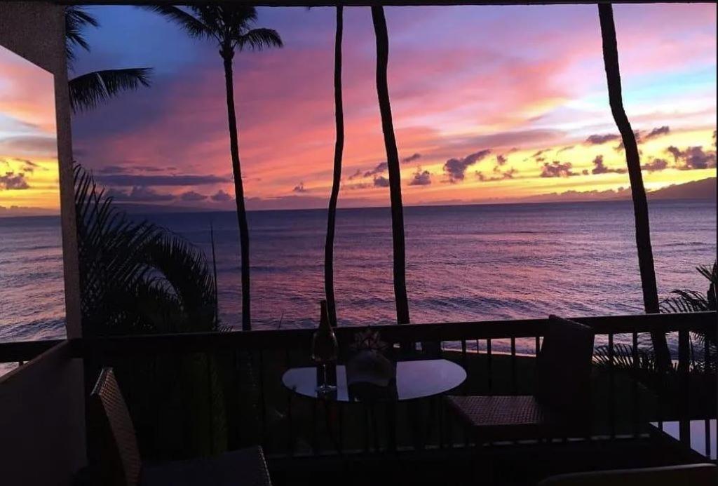 a person sitting at a table on a balcony with a sunset at Oceanfront with Private Beach! Hale Mahina Beach Resort A206 in Lahaina