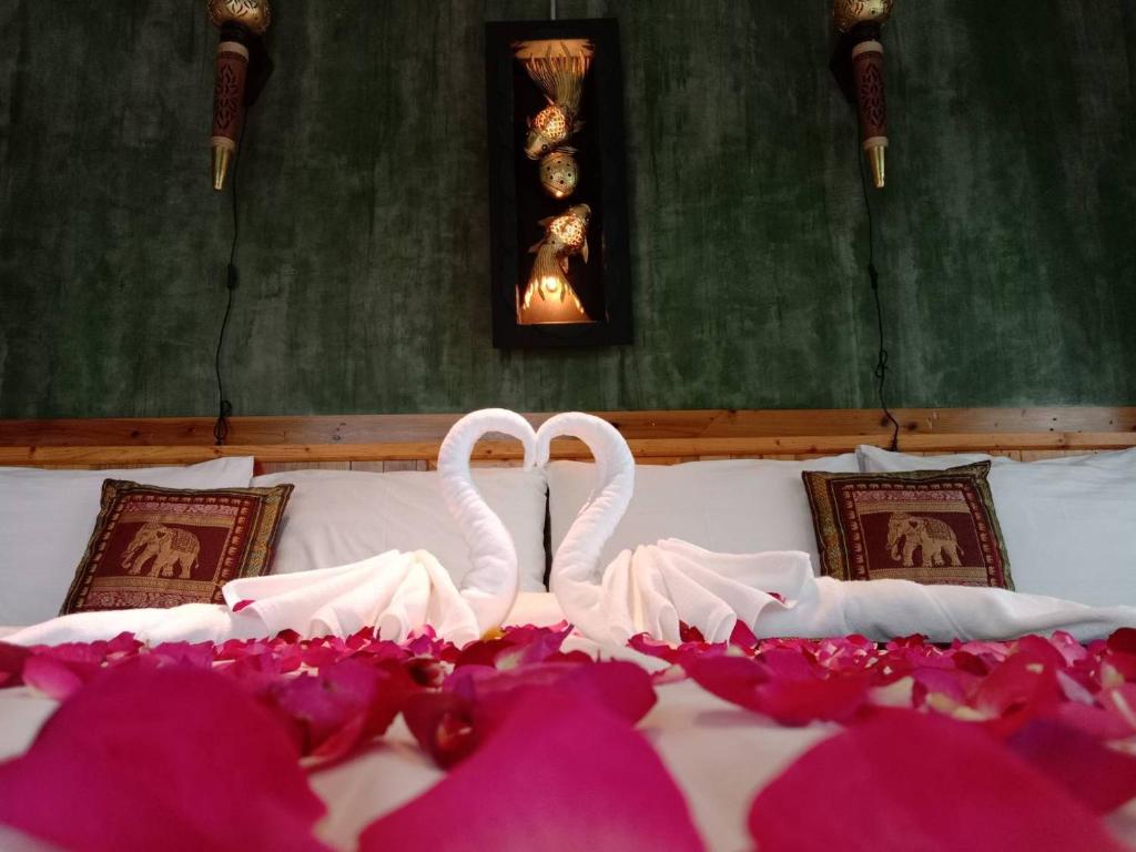 two white swans sitting on a bed with pink flowers at Keeree at chiewlarn in Ban Tha Khun