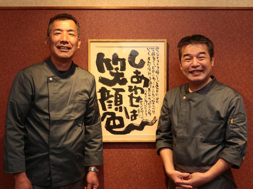two men standing in front of a wall with a painting at 港の魚宿 おおそね in Owase