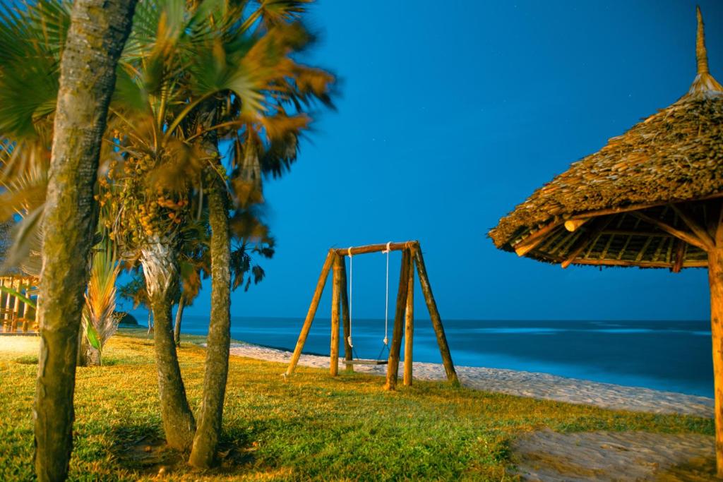 a swing and a straw umbrella on a beach at Amani Beach Resort in Dar es Salaam
