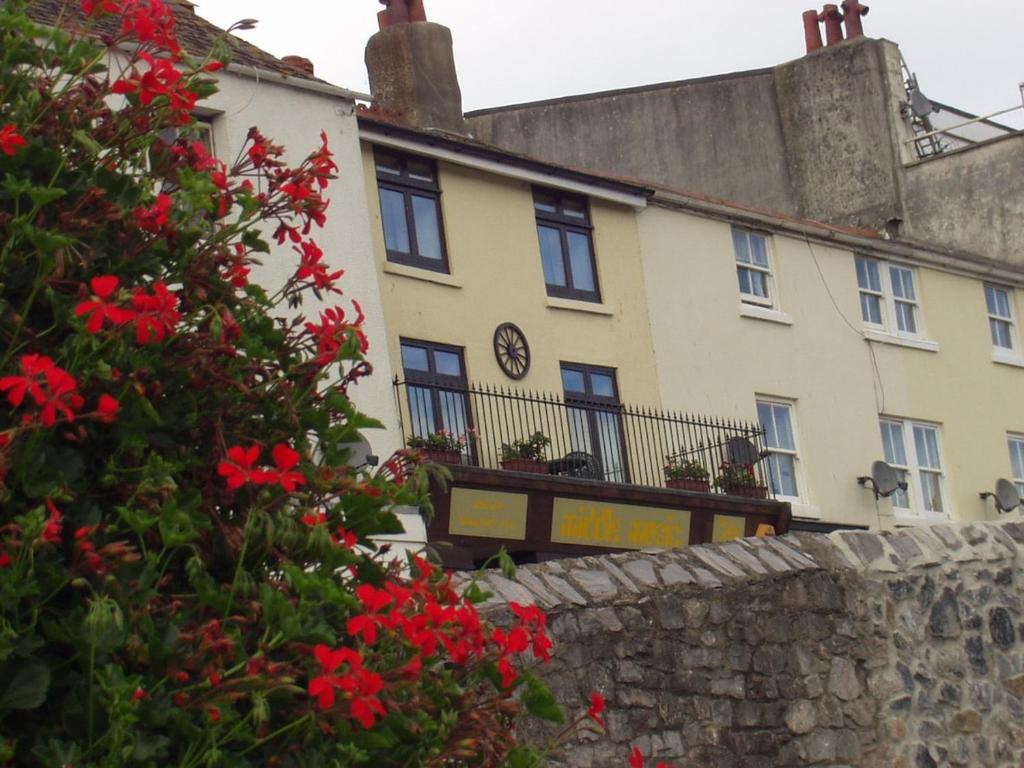 a building with red flowers in front of a wall at Upper Cottage, Brixham in Brixham