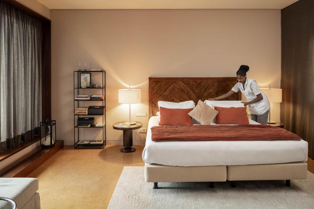 A contemporary bedroom with a padded bed, open shelving, and a person styling the pillows.