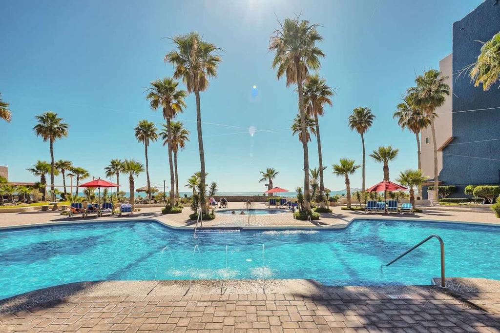 a swimming pool with palm trees in a resort at Cozy Ground Level Condo near Pool Pinacate 112 in Puerto Peñasco