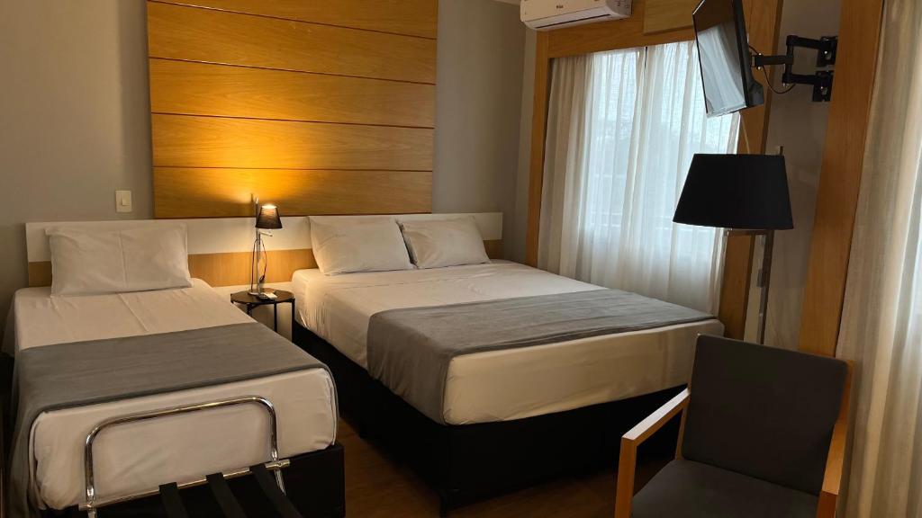 a hotel room with two beds and a window at Suíte Aeroporto Congonhas Quarto Triplo in São Paulo