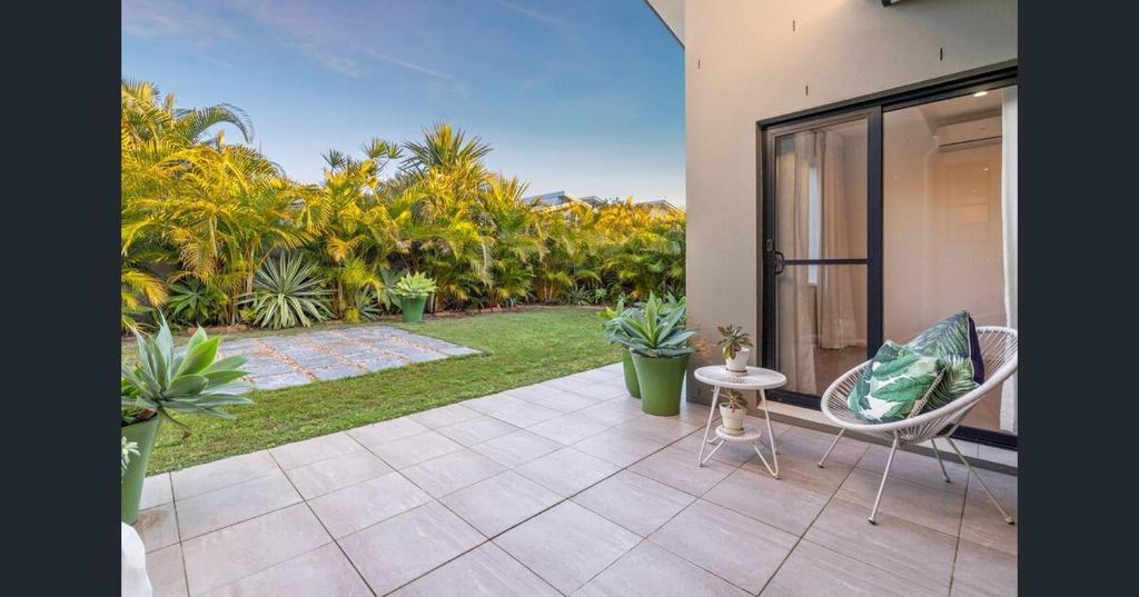 a patio with chairs and a yard with palm trees at Longboard Coastal Retreat in Kingscliff