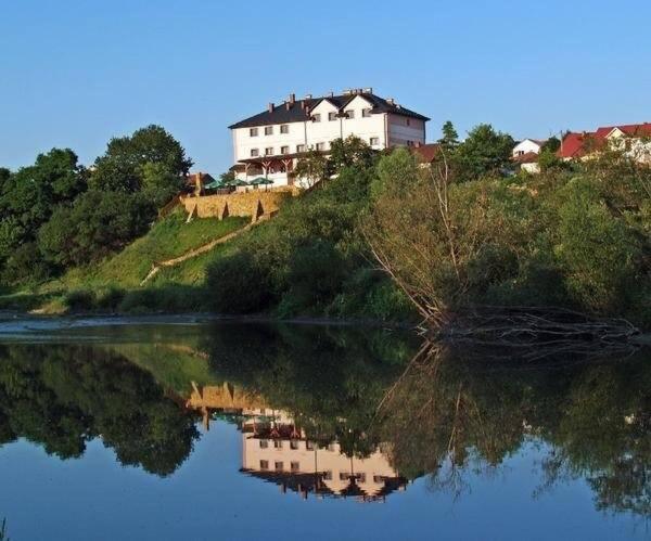 une maison sur une colline à côté d'une masse d'eau dans l'établissement Hotel Bursztynowy, à Józefów na Wisłą