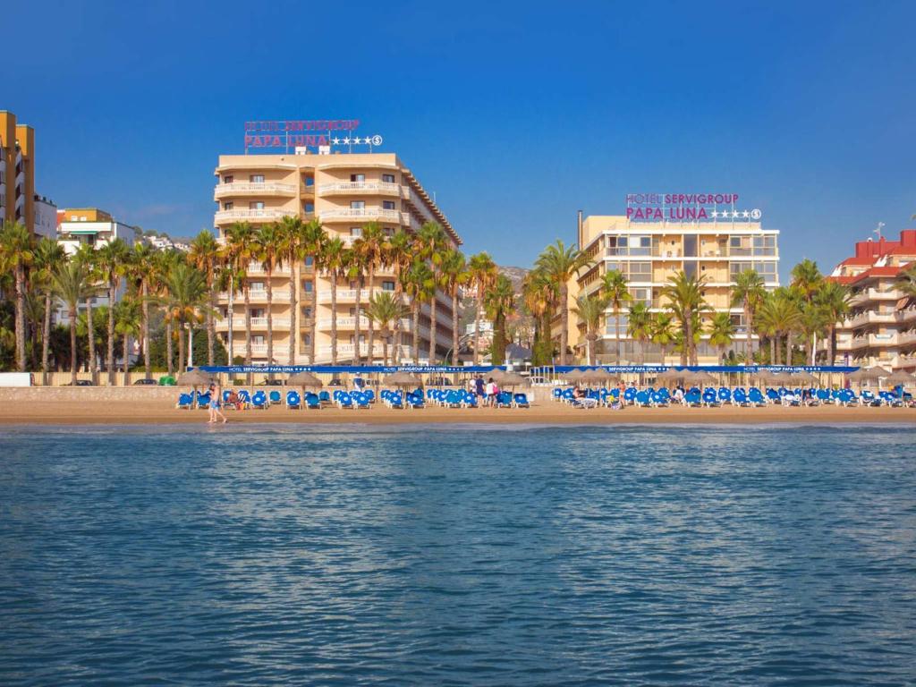 a beach with chairs and palm trees and buildings at Hotel Servigroup Papa Luna in Peniscola