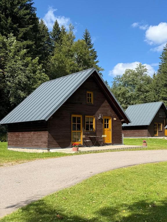 a small wooden house with yellow doors and a road at Chalets & Apartments - Base Camp Medvědín in Špindlerův Mlýn