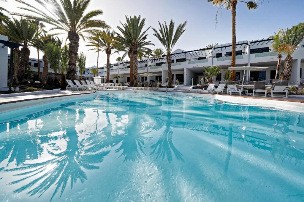a large swimming pool with palm trees and a building at BLUESEA Playa Club in Puerto del Carmen