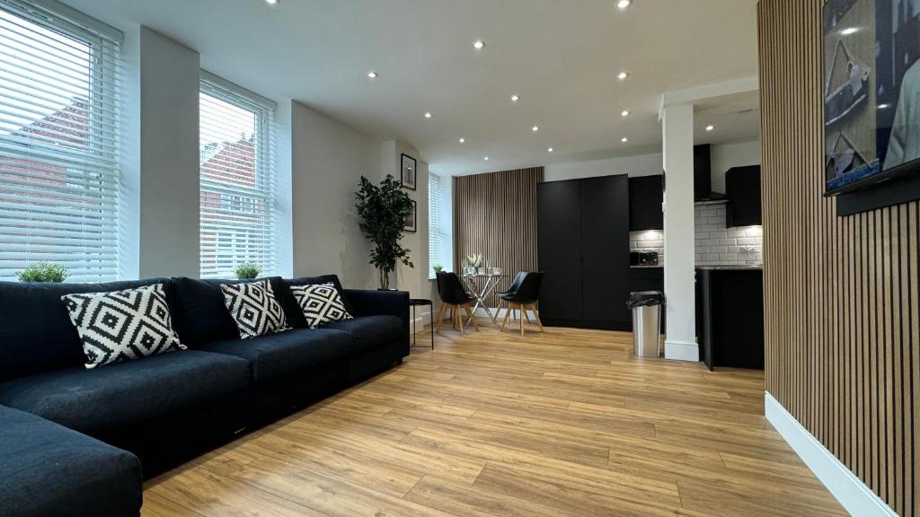 a living room with a black couch and a kitchen at Stylish 2 Bedroom Coastal Apartment near Crosby Beach & Liverpool in Waterloo