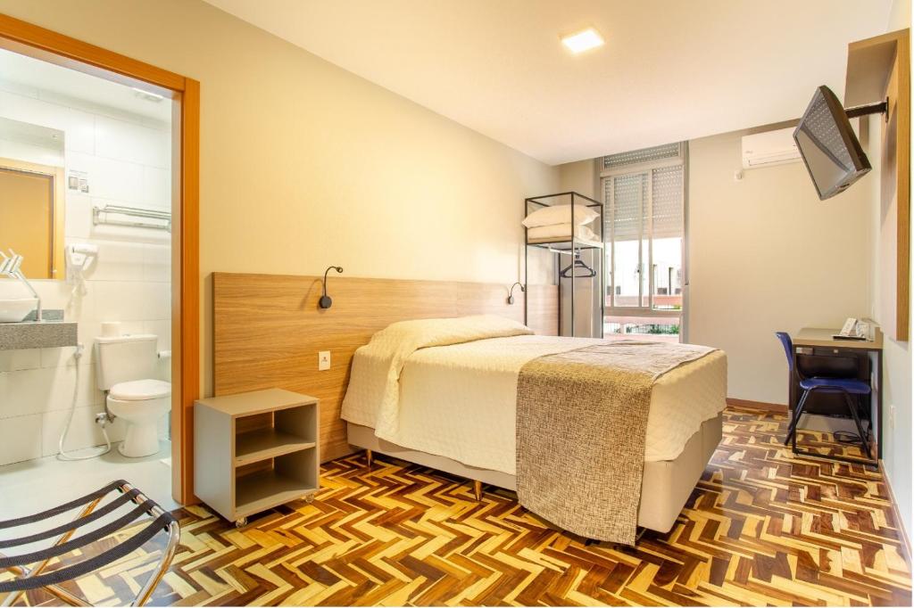 a bedroom with a bed and a desk and a bathroom at Hotel Dom Rafael Business in Santa Maria