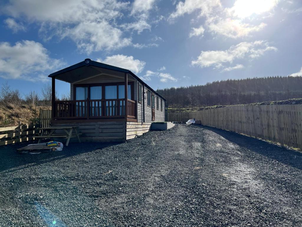 a small cabin on a gravel road next to a fence at Maneight Retreat with Hot tub in New Cumnock