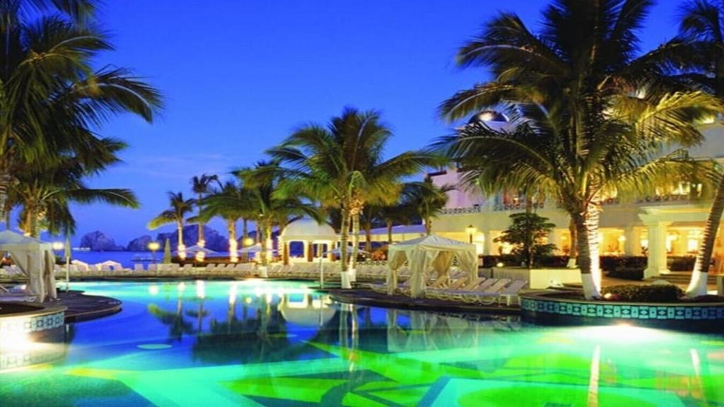 a swimming pool with palm trees and a building at Owners Studio Suite, REQUEST DATES- see by Clay & Lisa in Cabo San Lucas