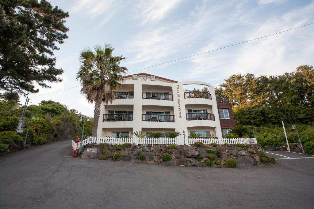 a white building with a palm tree in front of it at Four Season Pension in Seogwipo