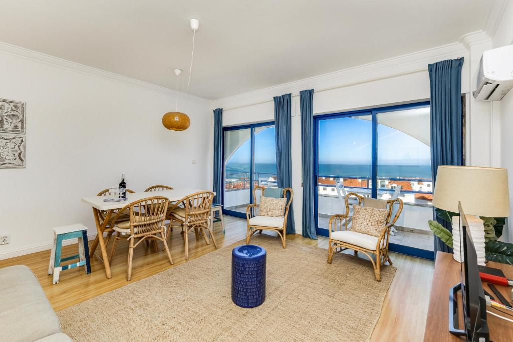 a living room with a table and chairs and windows at Apartamento Mar Salgado Ericeira in Ericeira