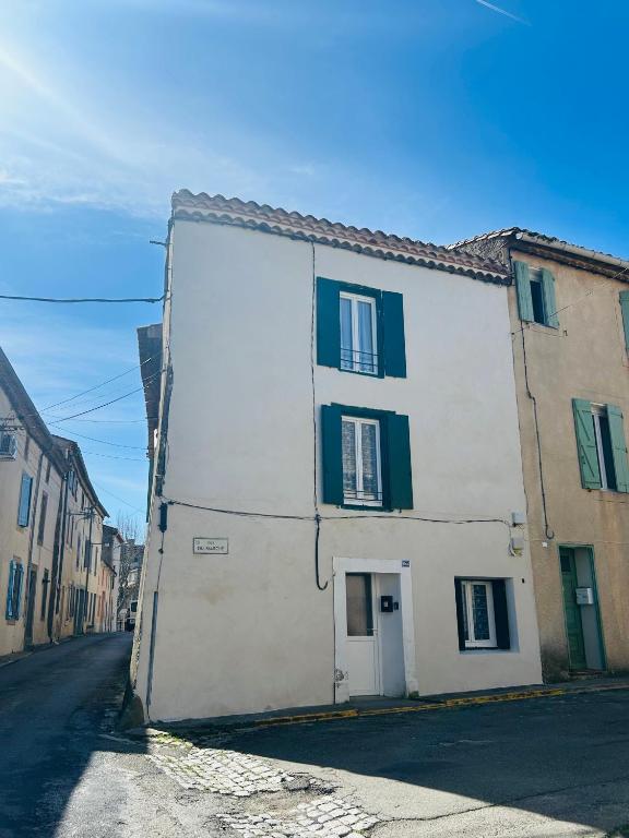 a white building with green shutters on a street at Maisonnette La Chouette in Azille