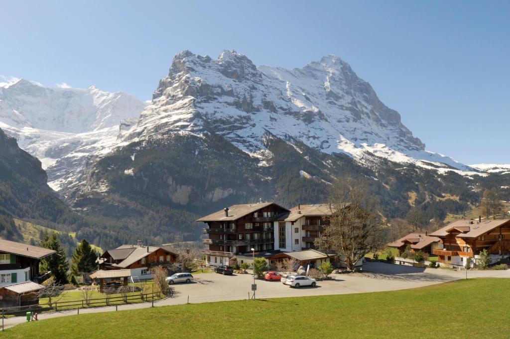 a snow covered mountain in front of a town with houses at Serviced Apartments – Kirchbühl@home in Grindelwald