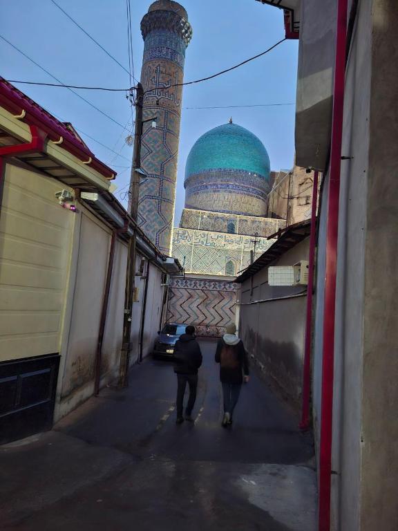 two people walking down a street in front of a mosque at Ramzan Family Guest House in Samarkand
