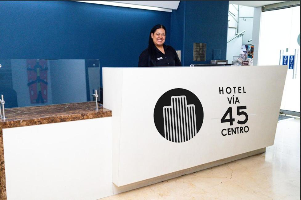 a woman is standing behind a reception desk at Hotel Via 45 Centro in Medellín