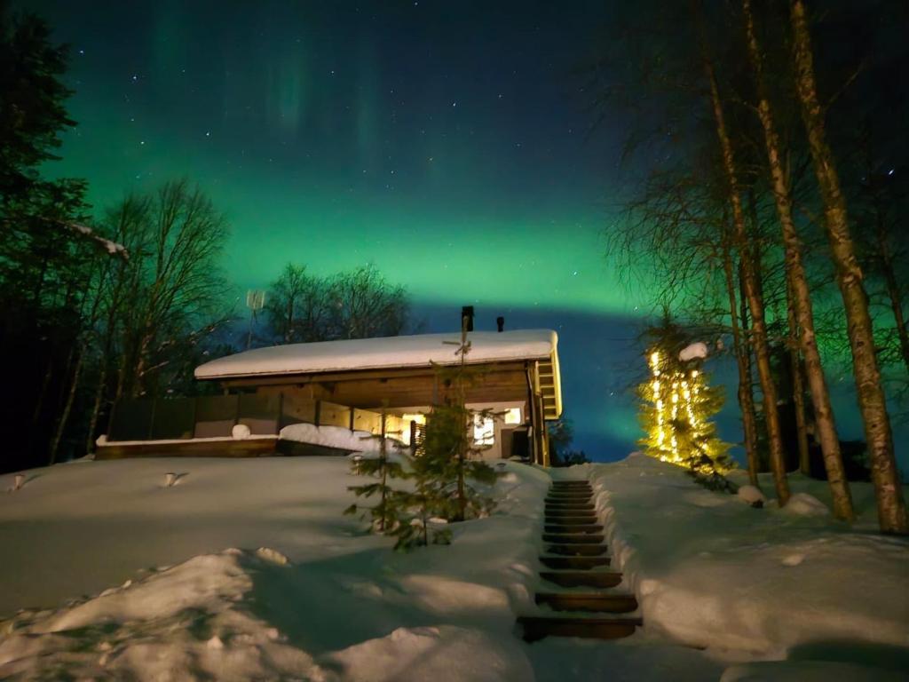 a cabin under the aurora in the snow at night at Villa lehto in Kuusamo