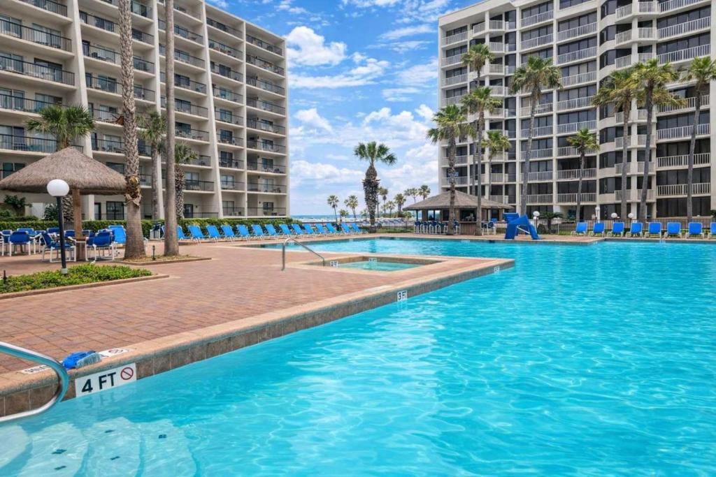 a swimming pool at a resort with blue chairs and palm trees at Beachfront Resort with Heated Pool Saida Royale 9039 in South Padre Island