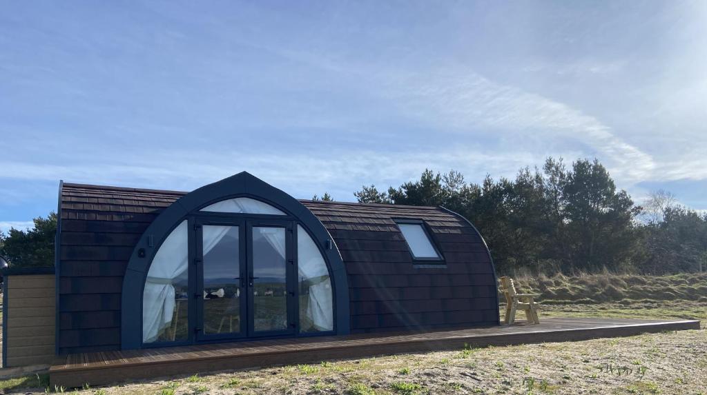 a small house with a large window in a field at Dornoch Pods in Dornoch