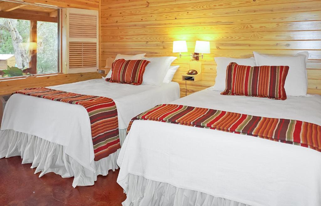 two beds in a room with wooden walls at Wimberley Log Cabins Resort and Suites- Unit 7 in Wimberley