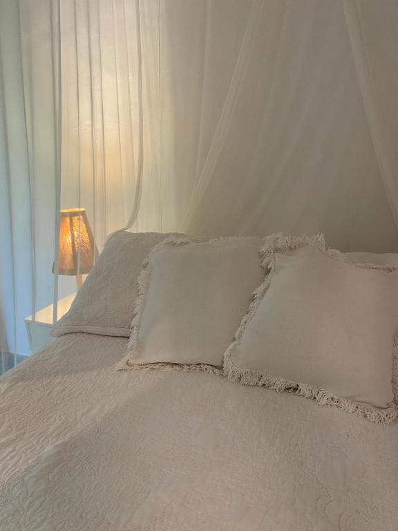 a white bed with white pillows and a lamp at Chalé Rosa in Trancoso