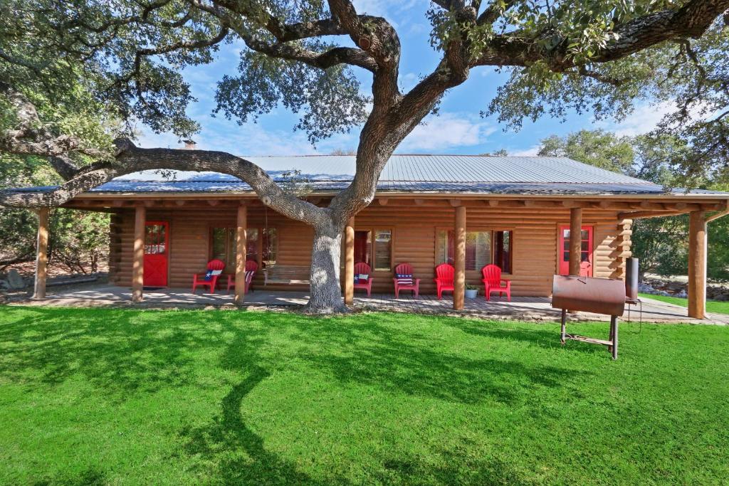 a log cabin with red chairs and a tree at Wimberley Log Cabins Resort and Suites- Unit 2 in Wimberley
