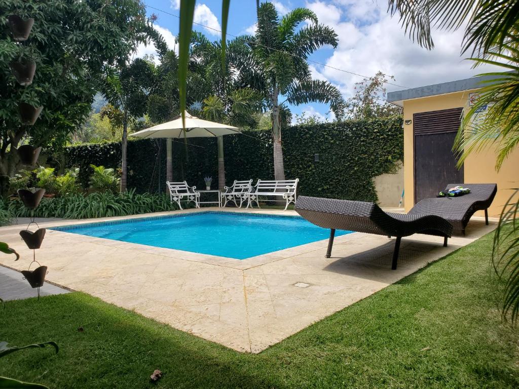 a swimming pool with chairs and an umbrella in a yard at Villa Rosalía con Piscina Climatizada in Jarabacoa