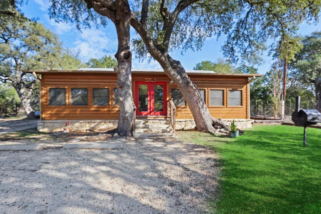 a log cabin with a red door under a tree at Wimberley Log Cabins Resort and Suites- Reunion Cabin in Wimberley