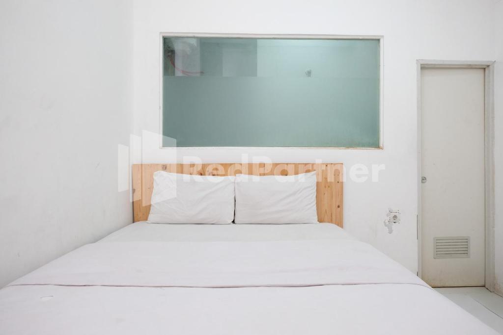 a white bed in a white bedroom with a window at Griya Aneka Malioboro Yogyakarta Mitra RedDoorz in Yogyakarta