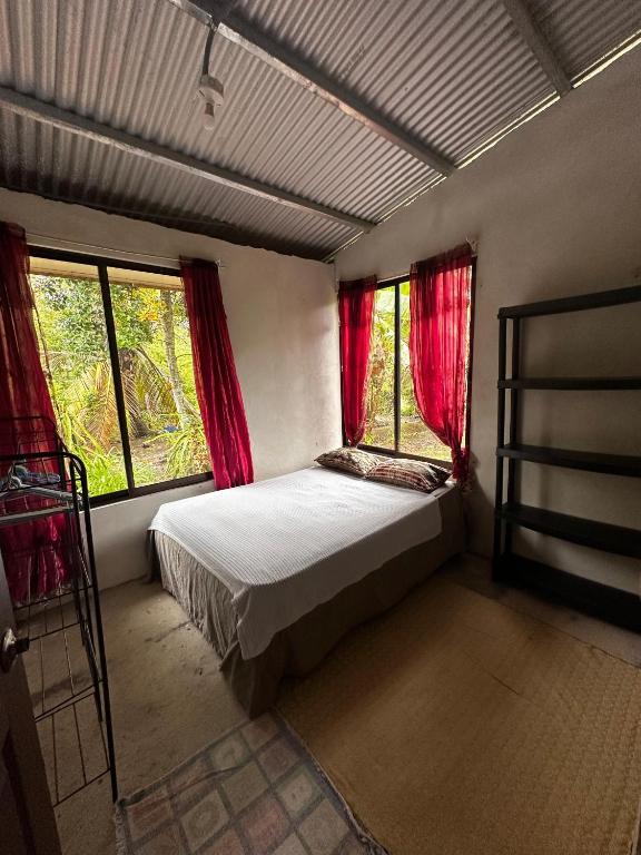 a bedroom with a bed and two windows with red curtains at Casa Rural Los Bufalos - Farm Stay in Guacimo in Guácimo