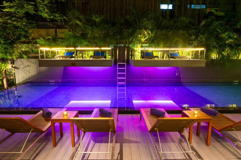 A purple-lit pool framed by loungers, candles, and tropical planting.