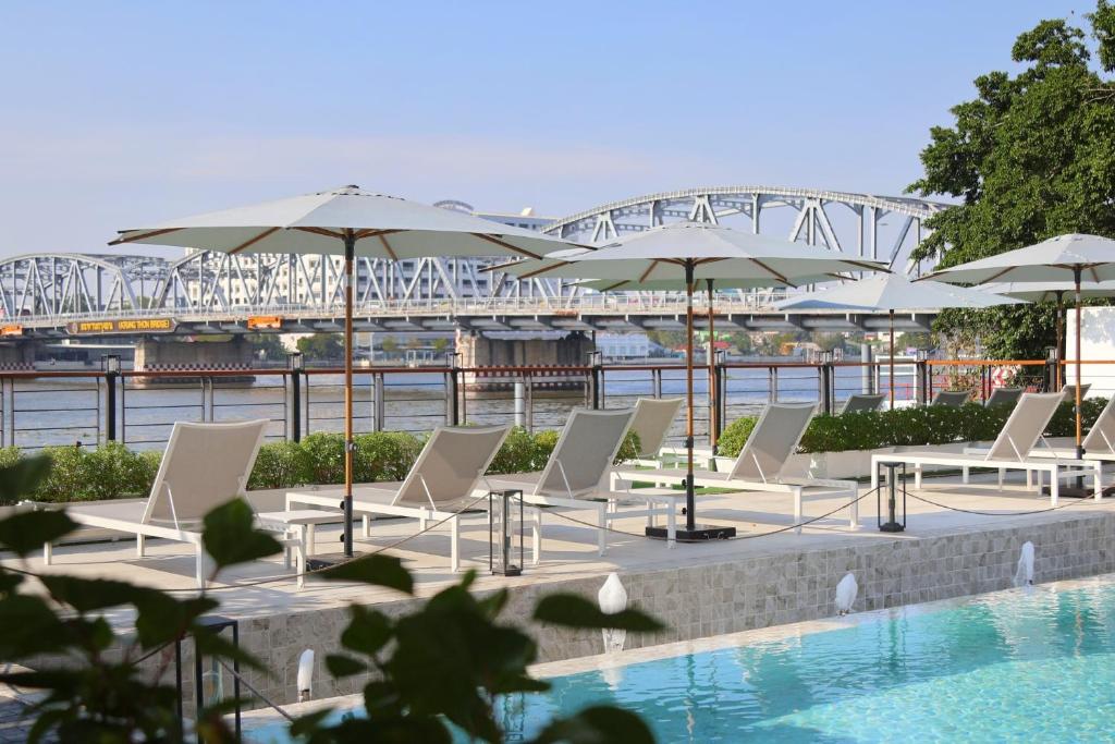 a group of chairs and umbrellas next to a pool at TARA Bangkok Riverside Formerly GLOW Bangkok Riverside in Bangkok
