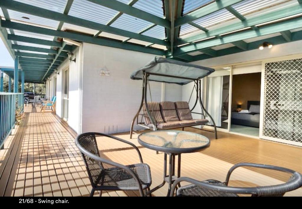 - une terrasse couverte avec une table, des chaises et une balançoire dans l'établissement Nest On A Crest, à Rye