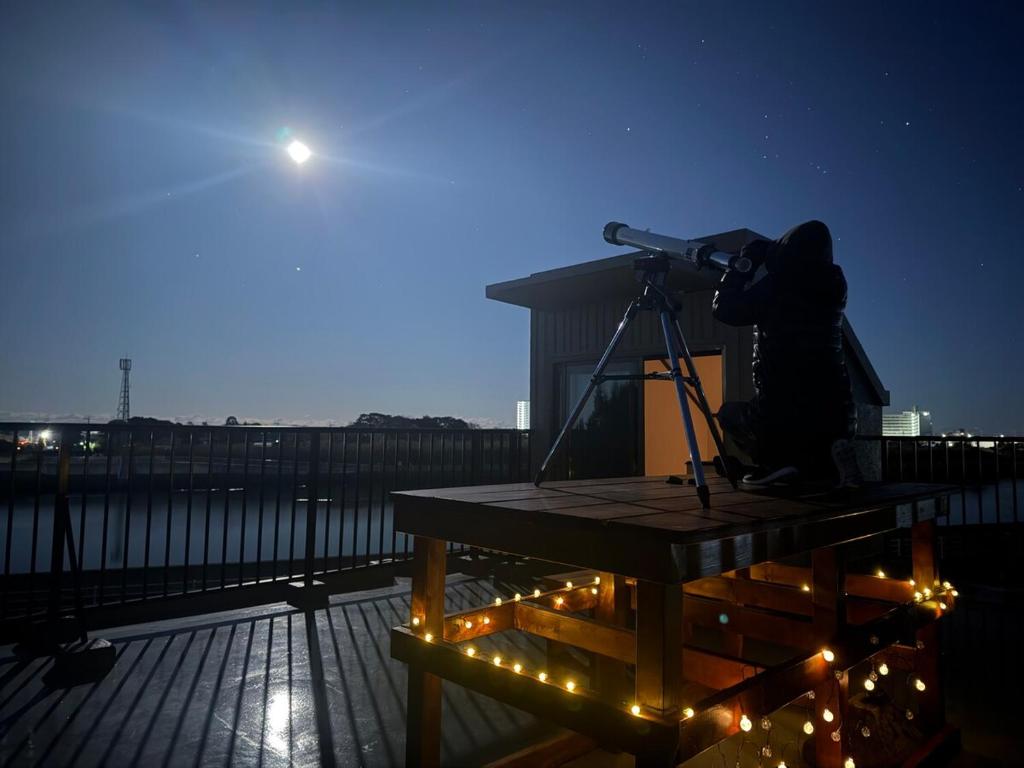 a person with a camera sitting on a table with a telescope at パノラマスター白子-Panoramastars Shirako-星降る夜の貸切ステイ in Shirako