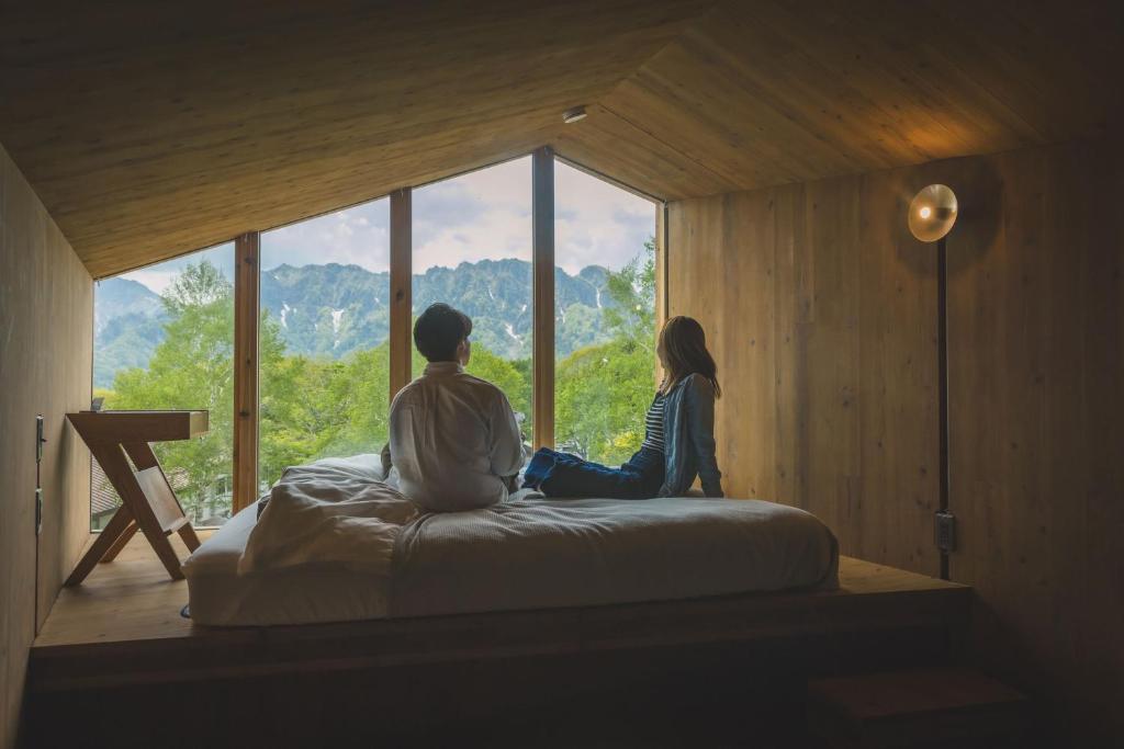a man and woman sitting on a bed looking out of a window at Earthboat Togakushi in Nagano
