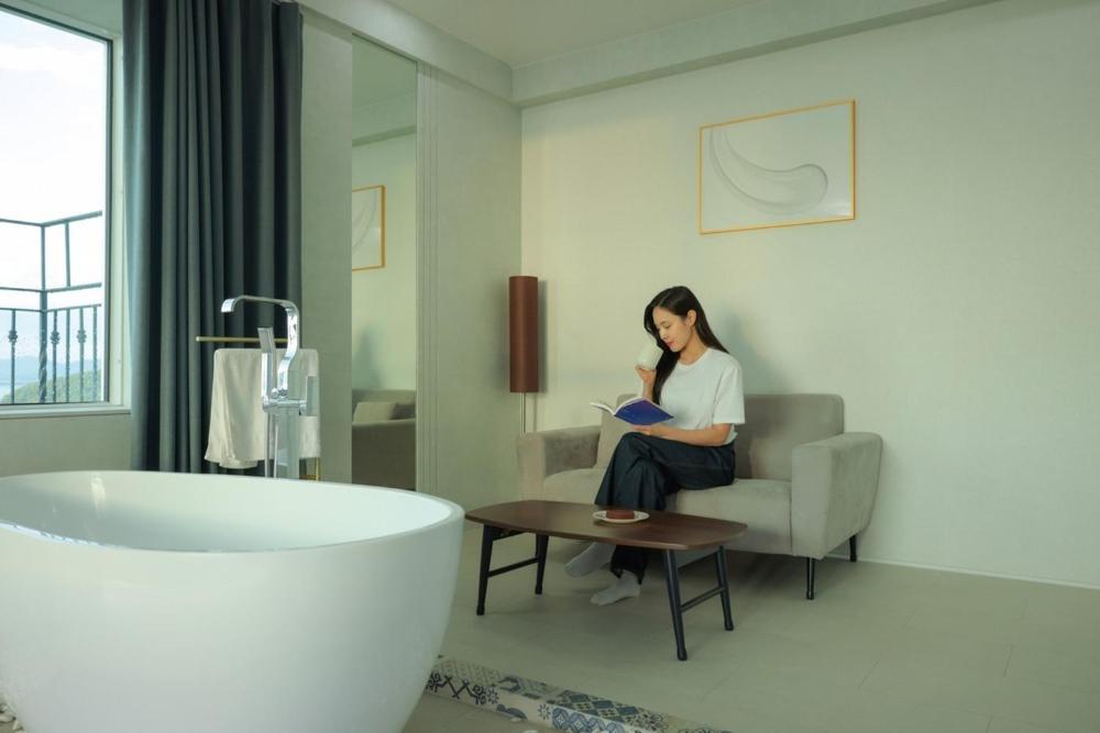 a woman sitting on a couch in a bathroom with a tub at CL Hotel in Boryeong