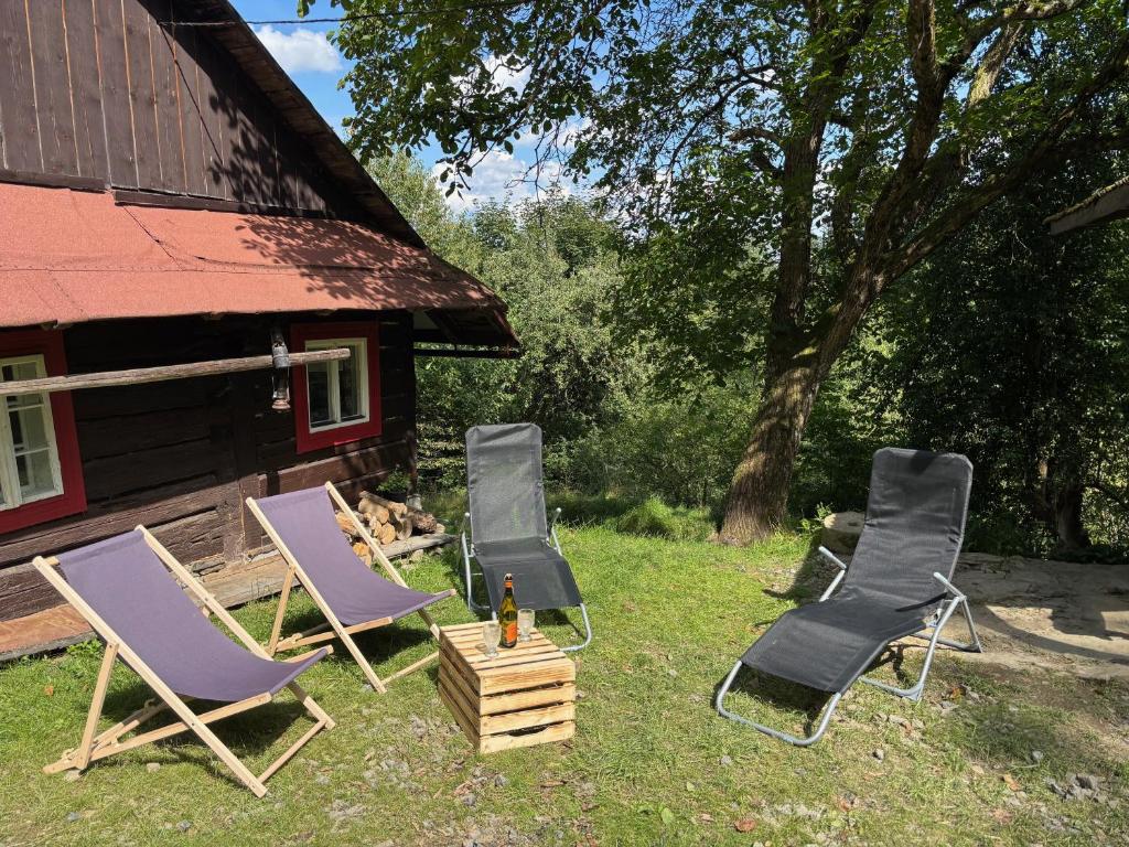 three lawn chairs and a bottle of beer in front of a cabin at Na samotě u lesa in Vsetín