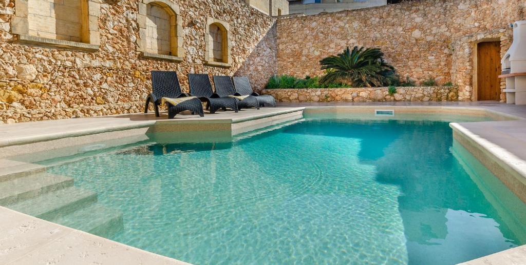 a swimming pool with chairs sitting in front of a building at Il-Kampnar Gozo Farmhouse with Private Pool in Sannat