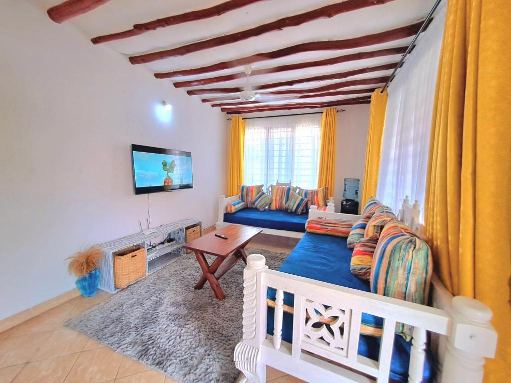 a living room with a blue couch and a tv at Elna's Haven Diani Palms - 5min walk to the beach, serene and culinary services in Ukunda