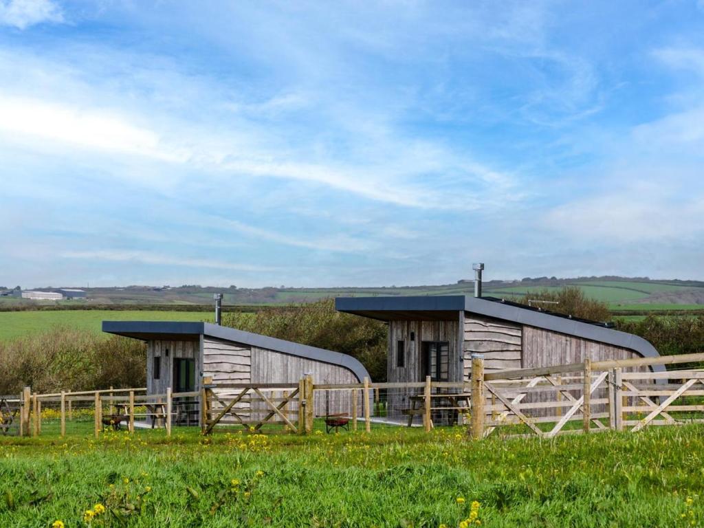two wooden buildings in a field with a fence at 1 Bed in Bude oc-88498 in Morwenstow