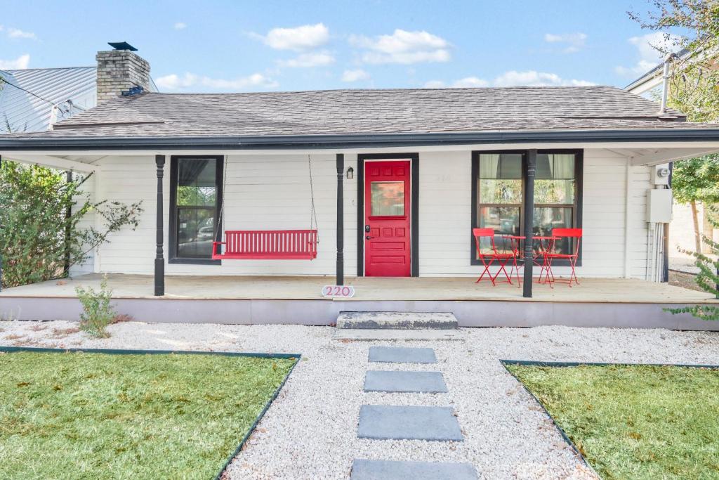 a white house with a red door and red chairs at The Tilted Texan in Buda